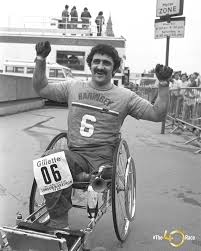 Athlete in a racing wheelchair leaning into a fast turn on a track, representing the rise of adaptive sports in the 1970s and 1980s