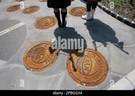 The shadow of Sandhogs Kevin Donohue, left, and Pete Ledwith are cast upon  manhole covers with names of the sandhogs who have died during the  construction of the city's third water tunnel