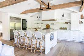 Chic country cabin kitchen features rustic wood beams and wood paneled walls concealing hidden pantry door. Spacious White Kitchen And Dining Area With Exposed Ceiling Beams Skout Hgtv