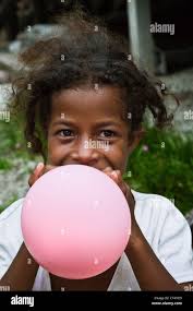 Indonesien, Papua Neu Guinea, Bonarua Dorf. Junges Mädchen bläst rosa Ballon  Stockfotografie