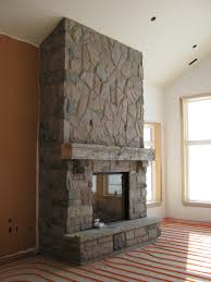 A whitewashed plaster and brick fireplace with firewood, a wooden mantel with candles and stacks of books. Custom Fireplace With Muskoka Granite Stone Rick Minnings Cultured Stone Work
