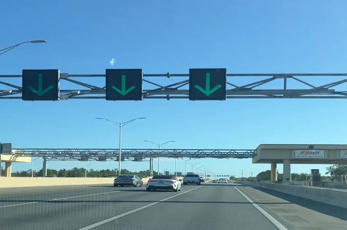Florida toll gantry over expressway with smartphone displaying online toll payment app.