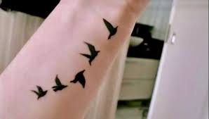 Little black birds flying alongside a dandelion plant on foot. 46 Birds In Flight Tattoos Ideas Tattoos Birds In Flight Tattoo Designs