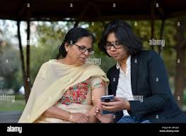 Smart young Indian girl with an old Indian woman looking at the mobile  phone and busy talking sitting on a bench in a park in Delhi, India Stock  Photo - Alamy