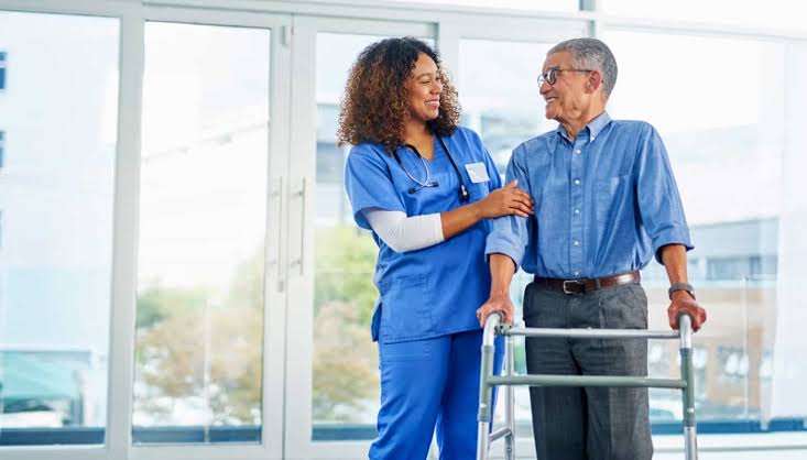 Nurse supporting an elderly patient using a walker in a clinic hallway