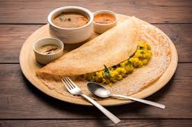 Golden crispy dosa folded on a plate with chutneys and sambar