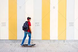 Check spelling or type a new query. Side View Of Teenage Boy In Headphones And With Backpack Skateboarding Down Paved Road Against Striped Wall Stock Photo Offset