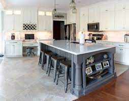 A frosted glass globe pendant hangs over a dark gray kitchen island lined with a stainless steel trim and topped with a white quartz. Cream Kitchen With Gray Island Lewis Custom Cabinets