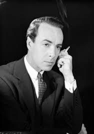 Carlos Navarro, actor, con cigarrillo encendido en mano junto a su rostro,  viste de traje y corbata, retrato | Mediateca INAH