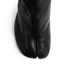 The features include a nubuck faux leather upper with a pointed closed toe, cut out scoop vamp, stitched trim, strappy design with buckle accents, lace up tie design, inner side zipper closure, smooth lining, and cushioned footbed. Maison Margiela Tabi Soft Leather Heeled Boots Black Hervia