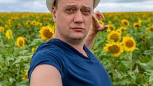 Парень в поле с подсолнухами на ферме в синей майке и в кепке