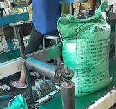 An industrial automated bagging line where large, lime-green woven sacks  are being transported via a conveyor belt system. Each sack is printed with  detailed product specifications and "Product ...