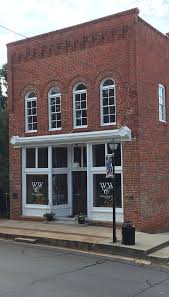 Four diverse women gathered around a wooden table, engaged in conversation, the background a warm tan hue. "Three blonde, ...