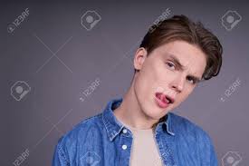 Close-up, A Young Fashionable Charming Sexy Boy In His 20s, With A Trendy  Stylish Hairdo, Seductively Stuck Out His Tongue And Playfully Looking  Straight, Posing On A Fmer Background. Stock Photo, Picture