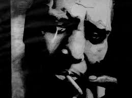 Howlin' Wolf poses for a portrait holding a box of matches that reads "Now  Smile", next to a bottle of Ancient Age bourbon, a box of Premium Nabisco  saltine crackers and a