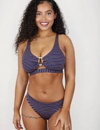 A girl in a swimsuit sits on a lounger and smears herself with sunscreen, the sun smiles and looks at her. 30 Best Swimwear Brands For Stylish Fun In The Sun Lh Mag