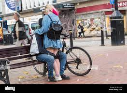 Ein paar junge Menschen zeigen eine öffentliche Zuneigung, während sie in  der Öffentlichkeit auf einer belebten Straße in Großbritannien kuscheln.  PDA. Mädchen mit nackten Beinen. Jeden Tag Stockfotografie - Alamy