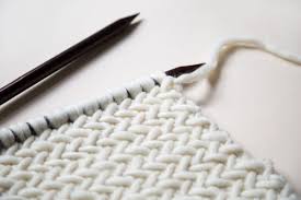Let's make sure you know how now, take your working yarn, which is in white in my example, and we are going to bring our working yarn all the way around to knit right into it. How To Knit Herringbone Stitch Wool And The Gang Blog Free Knitting Kit Patterns Downloads