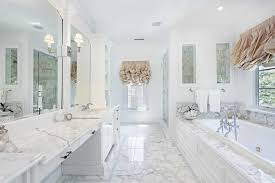 Spa like bathroom features a freestanding tub placed in the center of the room facing a french linen tufted bench placed under a window. White Bathroom Designs That Will Inspire Your Next Renovations