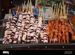 Asian street food - Long sticks with squid and meat Stock Photo - Alamy