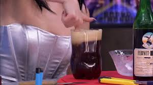 Fernet viajero servido en una botella pl&aacute;stica cortada, con espuma arriba, junto a una botella de Fernet Branca y una hielera, en una mesa.