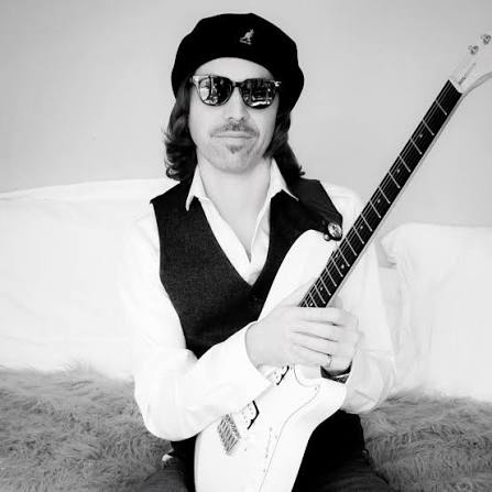 Jeffrey James Horan seated with an electric guitar in a black and white studio portrait