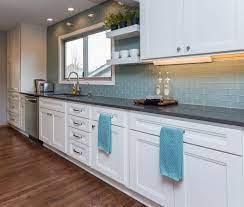 The focal point of this beautiful kitchen is the stunning stainless range hood accented with antique gold strapping. White Cabinets And Gray Quartz Countertops Are The Perfect Neutrals For This Blue Backsplash Blue Backsplash Gray Quartz Countertops Grey Countertops