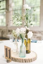 Small Floral Arrangements In Used Wine Bottles On Tables Atop A Round Slice Of Round Wedding Tables Cheap Wedding Table Centerpieces Wedding Table Centerpieces