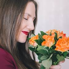 Primer plano de una niña sosteniendo un ramo de rosas naranjas frente a  ella y oliéndolo