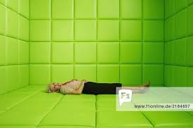 Frau in einer Ecke in einer grün gepolsterten Zelle geduckt