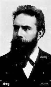 Black and white, headshot photograph of scientist, and discoverer of the X-ray,  Wilhelm (or Willam) Conrad Rontgen, with a bushy beard, and wearing a dark  suit, looking off camera, in three-quarter profile