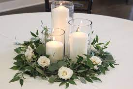 Using seasonal large flowers and candles is a smart idea to minimize spending on wedding table decor and summer home decorating. Greenery And Spray Rose Centerpiece With Pillar Candles Celebration Flair Wedding Table Centerpieces Candle Centerpieces Romantic Candle Centerpieces