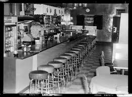 The high seating and low footstool make a comfortable seat for those summer evenings. Interior View Of Bar Or Club With Bar Stools And Checkered Floor With Cigarette Machines In Background And Upright Cooler Behind Bar Filled With Beer Cmoa Collection