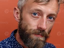 uma homem com curto cabelo e uma barba olhares fixos diretamente, vestindo  uma vermelho xadrez camisa. dele expressão é calma e considerado, com uma  suave foco em a face contra uma sutil