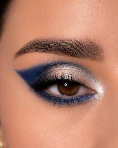 Close-up of an eye featuring bold blue eyeshadow, smoky eyeliner, silver shimmer and dramatic lashes

