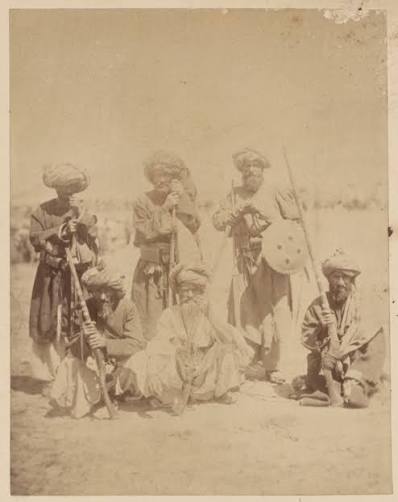 Photograph of the Khan of Lalpura, the leader of the Lalpura region of Afghanistan, and his followers on a mountainside. The Khan is standing in the middle of a group of Afghan