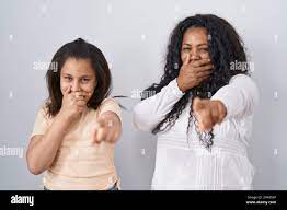 Mother and young daughter standing over white background laughing at you,  pointing finger to the camera with hand over mouth, shame expression Stock  Photo - Alamy