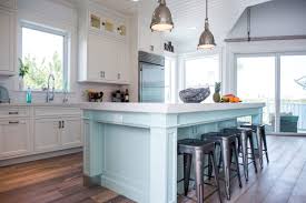 Coastal farmhouse kitchens make use of plenty of bright whites and reclaimed woods, apron style sinks and lantern pendant lights. Coastal Style White Kitchen With Blue Island Crystal Cabinets