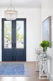 Flanking a white scalloped mirror, light blue double gourd lamps sit on a white credenza placed on charming tan and blue foyer is covered in white and blue wallpaper and accented with a round blue. Reveal Casual Cool The Guest House Studio Stairs Design Interior Front Door Entryway Front Entrance Decor