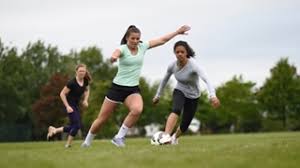 Young family chasing after a football in a family in park riding on roundabout. Play Women S Football Get Involved Women S Girls The Football Association
