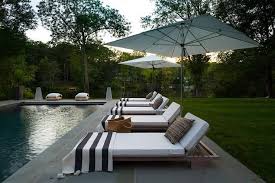 Black And White Striped Pool Umbrella Teak Pool Loungers Accented With White Cushions Sand Black And White Stripe Towels Sit On Slate Pavers Beneath Wh Pool Lounger Beautiful Outdoor Spaces Outdoor