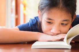 El Niño Lee El Libro En La Mesa Imagen de archivo