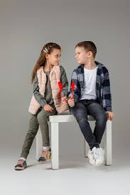Premium Photo | Cute stylish little couple child girl and boy with red  hearts on stick in fashionable clothes sittting together