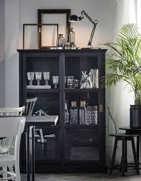 In A Dining Room A Glass Door Cabinet Holds Glasses Plates And Decorative Pieces A Lamp Glass Bottles And Empty Fr Glass Cabinet Doors Home House Interior