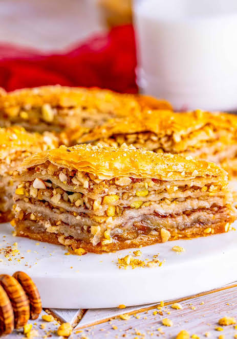 Fresh ingredients for homemade baklava recipe including phyllo dough, pistachios, butter, and honey on a wooden table