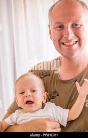Father holding in right hand his crying, four months baby Stock Photo