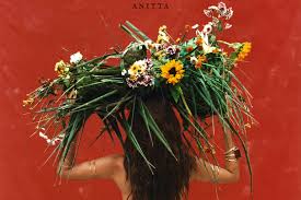Anitta carrega um grande arranjo de flores e folhagens sobre a cabeça em capa de álbum com fundo vermelho.