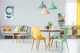 Even if you think a dining room is a great place to experiment with color, that doesn't mean you have to pick a bold wall color; Modern Colorful Chairs At Dining Table Under Pastel Lamps In Living Room Interior With Pillows On Settee Against Wall With Poster Stock Photo Picture And Royalty Free Image Image 93885502