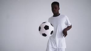 A Professional Black Football Player in a White Uniform on a White Background Juggles a Ball in Slow by petrunine