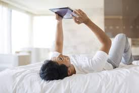The sec­ond sen­tence is in­cor­rect, un­less you are about to lay an egg. Chinese Man Lying Down With Digital Tablet On Bed Domestic Life Bedroom Stock Photo 178424000